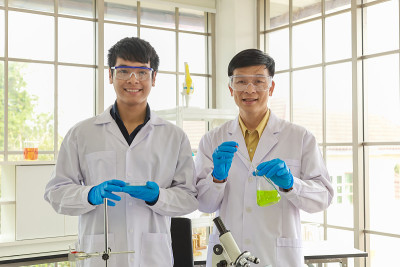 在工作实验室中，专业的资深和年轻的博士科学家手拿装有绿色液体物质的培养皿和锥型烧瓶。