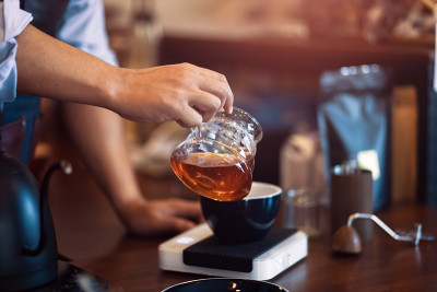 咖啡师拿着蘸汁杯，将蘸汁后的热咖啡倒入一杯咖啡中。