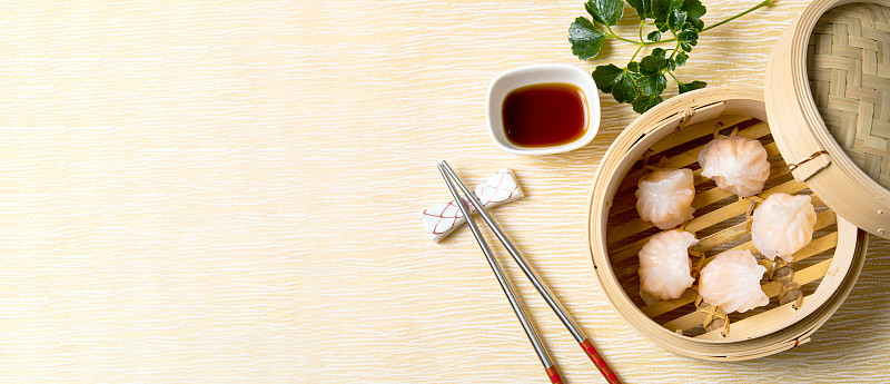 蒸虾饺，配酱料和筷子。中国传统美食的概念。饺子点心在竹蒸笼内用文字抄写空间。亚洲食物背景