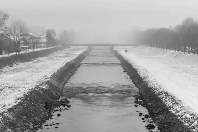 寒冷，雾蒙蒙的黑白景色，一条河和一个散步和远处的人享受雪