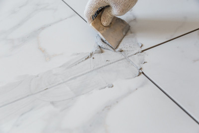 Grouting tiles seams with a rubber trowel.