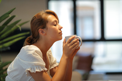 一个女人在家里闻咖啡杯的侧面图