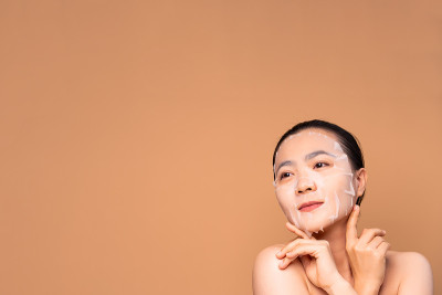 亚洲妇女的肖像与面部面具站在孤立的米色背景。