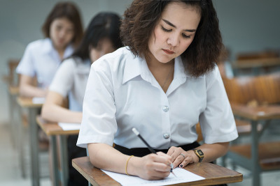 选择性焦点的青少年大学生坐在讲座椅上做期末考试和写在试卷上的答题卡在教室里。大学生在教室里穿制服。