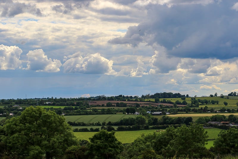 俯瞰爱尔兰米思县(County Meath)肥沃的乡村农业景观，在夏天，它被郁郁葱葱的树篱和上方蓝色