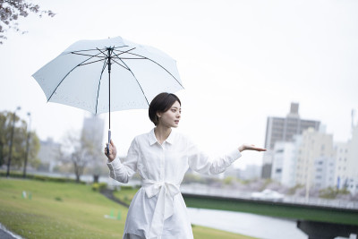 一个穿着白色连衣裙的年轻女子撑着伞在雨中行走