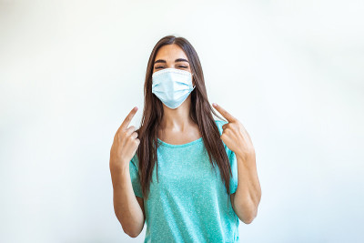 冠状病毒爆发:一名妇女用一次性医用口罩避免传染性病毒，手指指向口罩。冠状病毒预防。冠状病毒隔离的概念