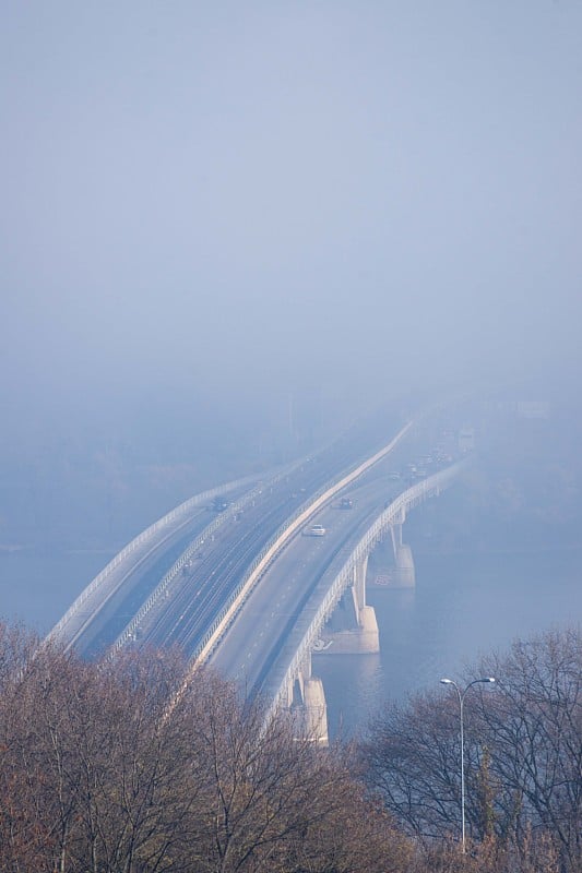 秋天的雾和河钢桥与地铁列车模糊的背景。森林在前景。