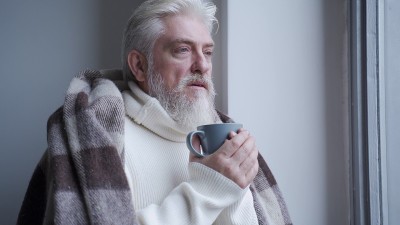 一位老人盖着温暖的毯子望着窗外喝着咖啡