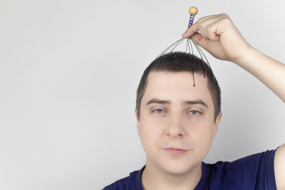 一个白色背景的男人用毛细管按摩器给自己做头部按摩。自助、抗压、放松理念