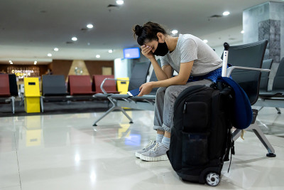 由于航班延误、错过或取消，带着医用口罩的紧张、疲惫或心烦意乱的女旅客坐在机场或火车站