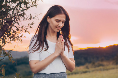 一个单身女人的肖像，祈祷着，看着夕阳。双手合十祈祷的观念，信仰，灵性和宗教。