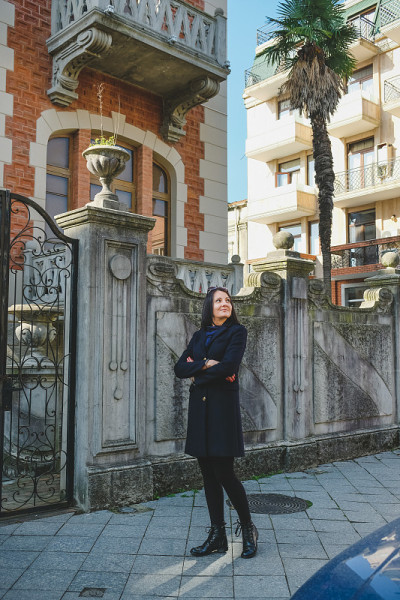漂亮的黑发女人穿着黑色外套走在老城里。