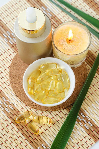 小的白色碗装化妆品油(清洁油，鱼油)胶囊，瓶子装血清和燃烧的蜡烛。天然水疗，皮肤和头发治疗配方。