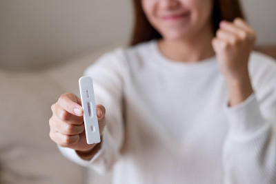 一个快乐的女人展示抗原检测试剂盒或快速检测设备的阴性结果