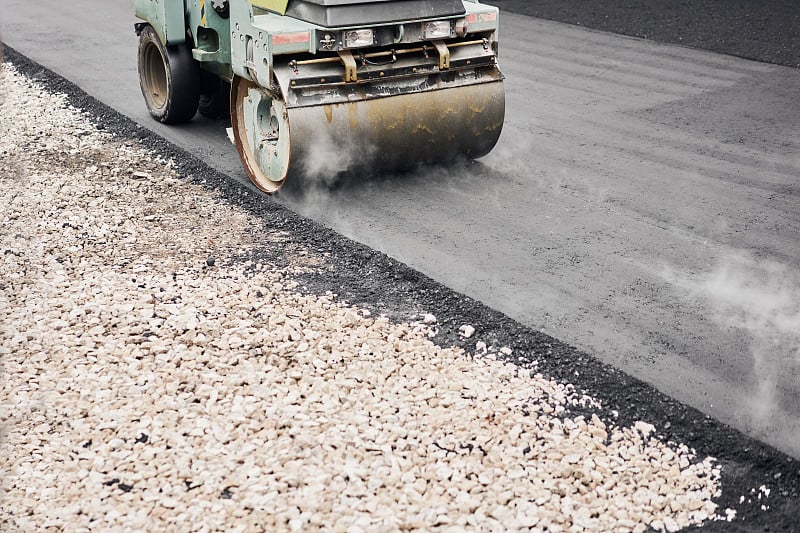 沥青压实机正在进行道路维修工作。新沥青铺设。大型重型机械。修建一条新的柏油路。