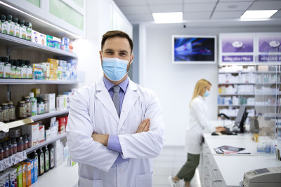 英俊的白人男性药剂师戴着面具站在药店里的肖像。