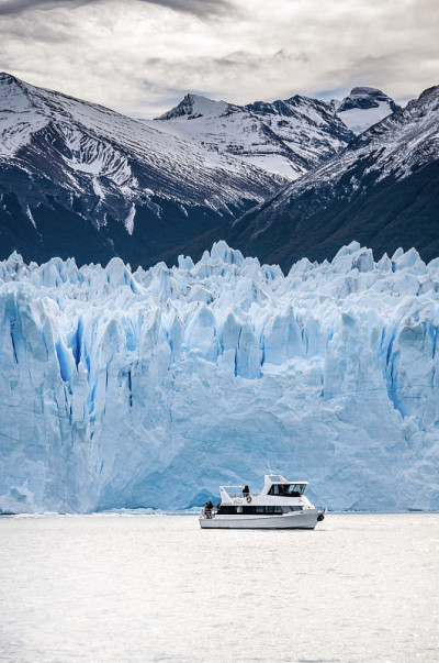 阿根廷巴塔哥尼亚El Calafate，一艘游船从佩里托莫雷诺冰川前经过。后面是白雪覆盖的安第斯山脉