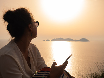 夕阳西下时，一名年轻女子在庞扎岛海岸的海边使用智能手机
