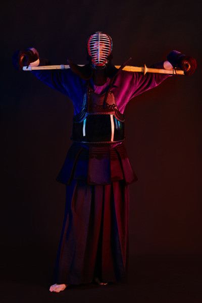 近景，剑道战士穿着盔甲，传统和服，头盔练习武术与shinai竹剑，黑色背景