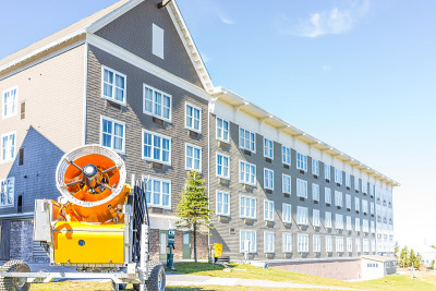 度假村小屋建筑和橙色造雪机与风扇叶片附近的滑雪场斜坡，秋天，秋天