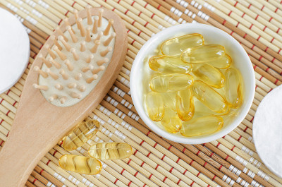 小的白色碗，装有化妆油(血清，鳕鱼油)胶囊和木质发刷。天然spa、护发美容配方。俯视图，复制空间。