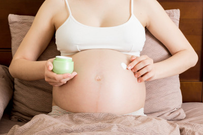 孕妇在腹部涂妊娠纹霜。怀孕、人与母性观念。孕妇在腹部涂抹抗妊娠纹霜