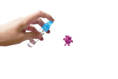 用手向紫色的冠状病毒或COVID-19雕塑用粘土喷洒消毒过的酒精或凝胶