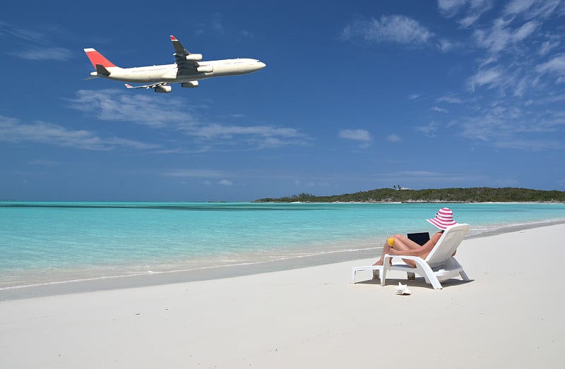 在热带海滩上拿着笔记本电脑的女孩。Exuma,巴哈马群岛