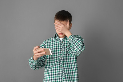 自由泳。男孩孤立地站在灰色的墙壁上，用手机遮住眼睛看视频