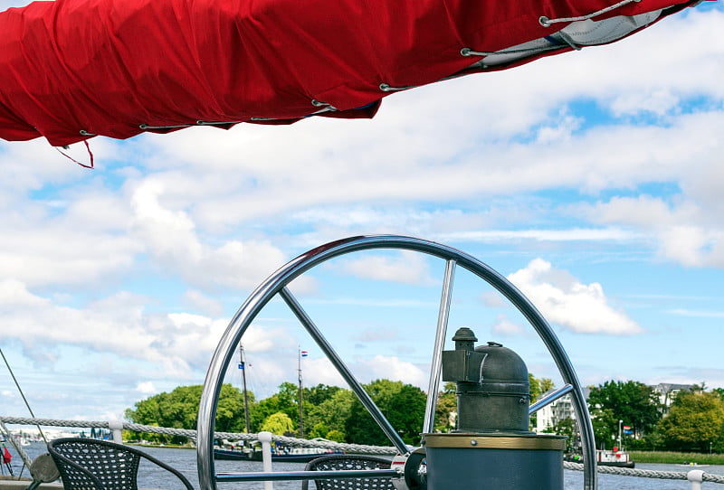 Steering wheel and red sails of tall ship against 