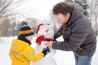 小男孩和他的父亲在下雪的公园堆雪人。冬季与孩子们一起进行户外活动。