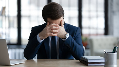 不高兴的商人坐在桌旁为生意失败而苦恼