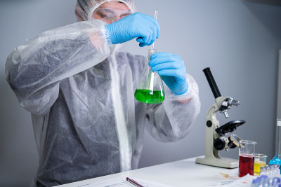 科学家摇动烧杯中的绿色液体。在实验室做测试或研究的年轻实验室助理。技术员测试化学实验室的实验和摇晃玻