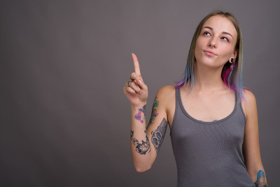 工作室拍摄的年轻美丽的女人与多颜色的头发和纹身穿着灰色背心对灰色背景