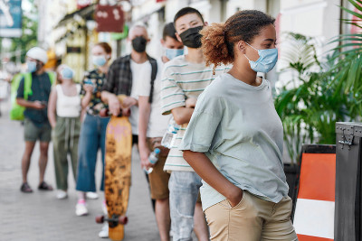 年轻的非洲裔美国妇女戴着面具等待，和其他人一起排队，在封锁期间尊重社交距离从接餐点领取外卖