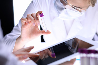 科学研究团队的特写，清晰的解决方案在实验室。金发女化学家拿着试管的玻璃，而她的同事用平板电脑检查结果
