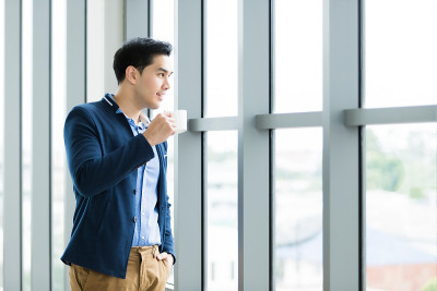快乐心情的肖像亚洲年轻商人工作拿着一个咖啡杯穿西装的男人在蓝色夹克和蓝色衬衫看着窗户在办公室的房间背