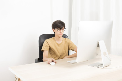 一个严肃的十几岁的男孩坐在椅子上，在家里用电脑。
