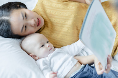 妈妈和她的儿子在睡觉前在床上看书。家庭故事的概念。