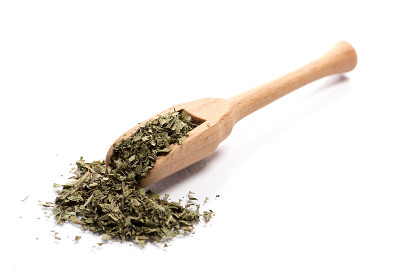 一堆干药草的特写，在一个木勺里的叶子在白色的背景