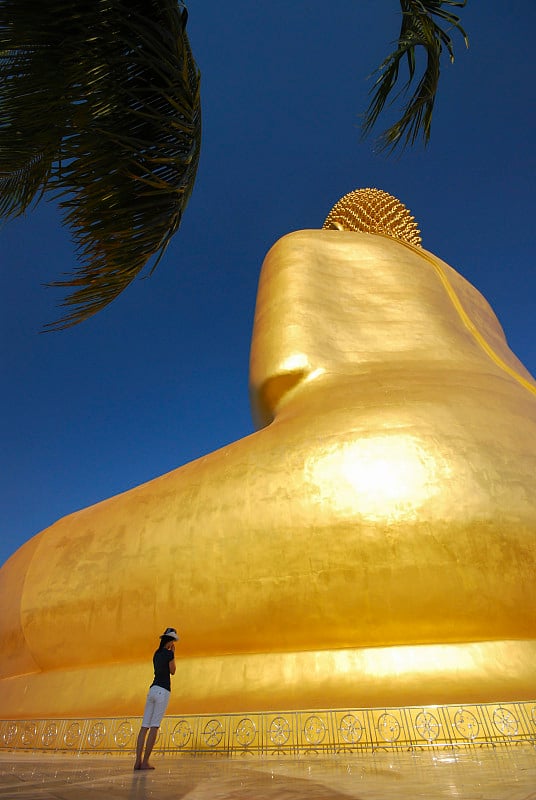 一名亚洲女游客正在泰国的芒寺为金色的大佛像祈福