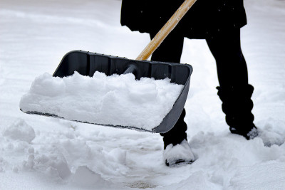 女性铲雪用铲子满雪，在冬天。