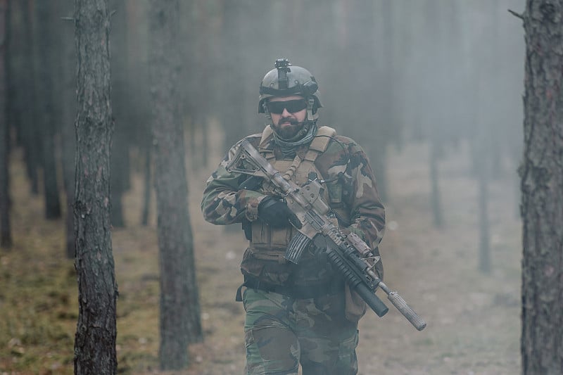 一名全副武装的士兵穿着迷彩服从松树林中的一股烟雾中走出来