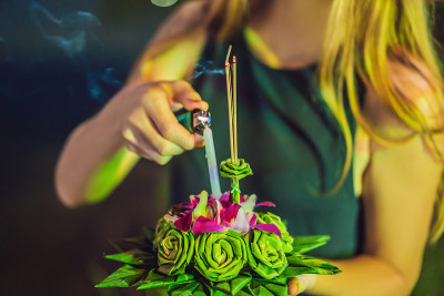 一名女游客手里拿着Loy Krathong，准备把它扔进水里。泰国的水牛节，人们购买鲜花和蜡烛点亮并
