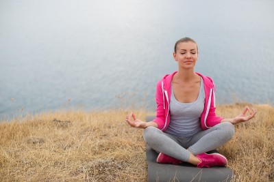 美丽的女人沉思在一个莲花的姿势在海洋岸边
