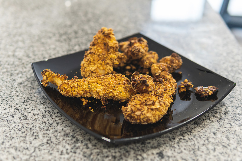 黑色盘子上的脆炸鸡胸和麦片