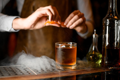 酒保在威士忌酒杯里挤橙子皮
