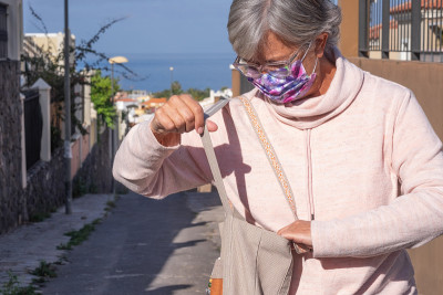 一位戴着防冠状病毒感染面罩的老年妇女在包里找东西