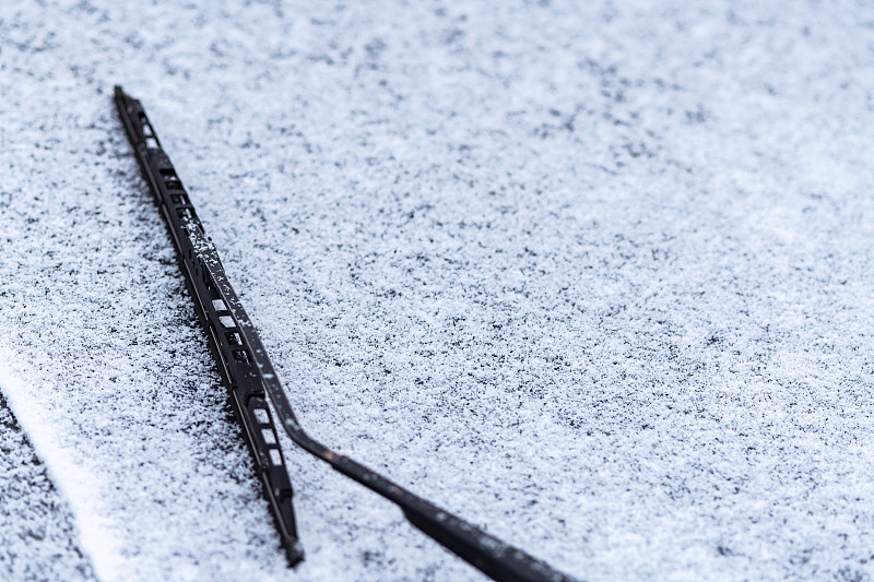 雪覆盖了车窗，用雨刷，微距，特写。没有使用防冻液。车辆在雪。冬天来了。恶劣的天气条件